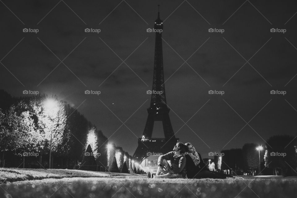 Couple sitting on grass near Eiffel Tower at night