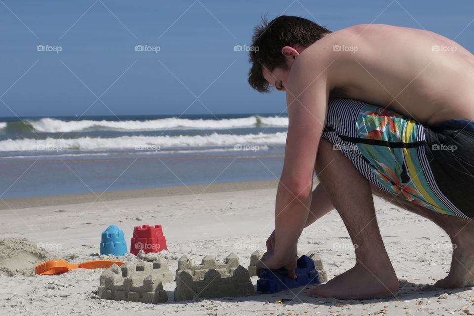Young Man Builds a Sandcastle on the Beach. Building a Castle on a Sandy Beach Near the Ocean.