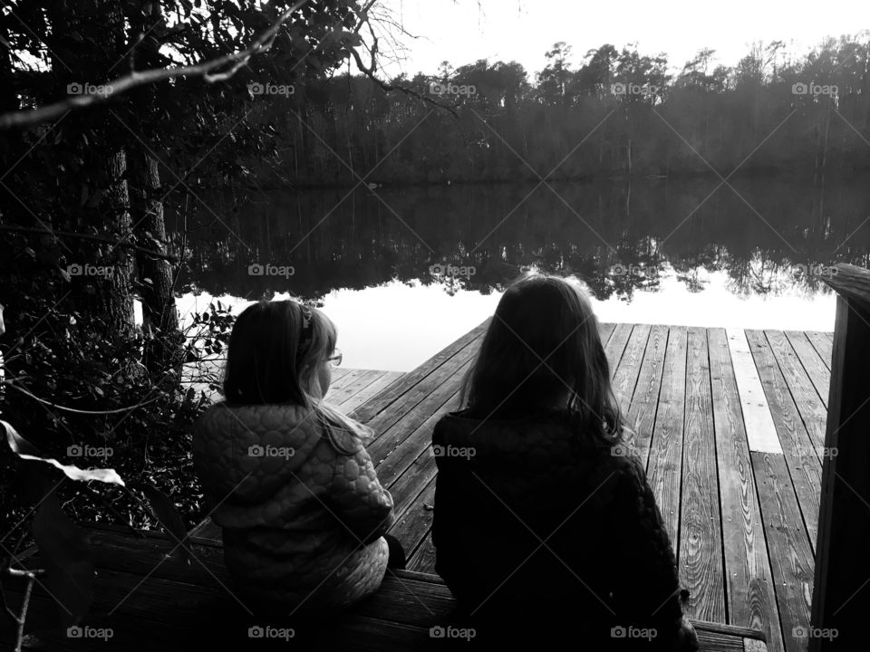 Sisters bonding at the dock of the pond at sunset 
