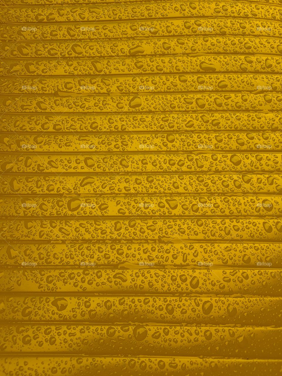 Close up of water droplets on a wet shiny plastic surface gold with horizontale lines parallele