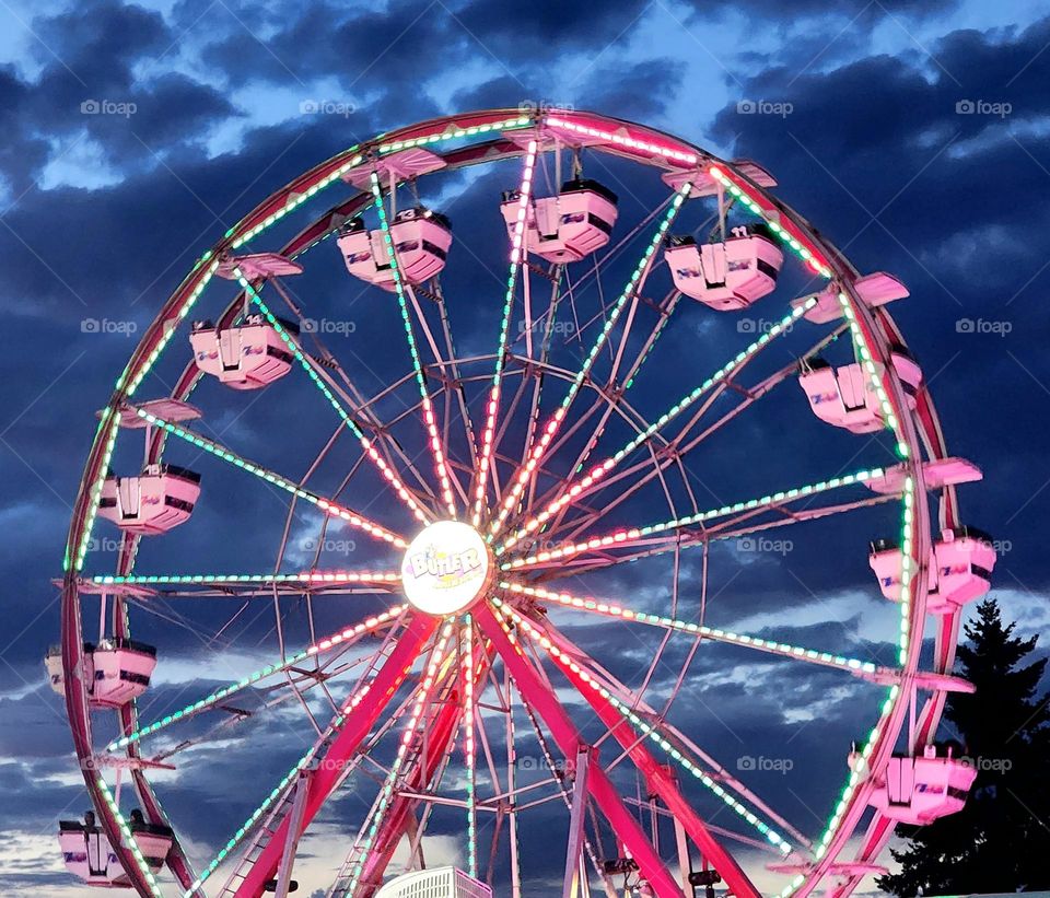 bright pink lit up Ferris wheel against dark cloudy night sky at a county fair in Oregon