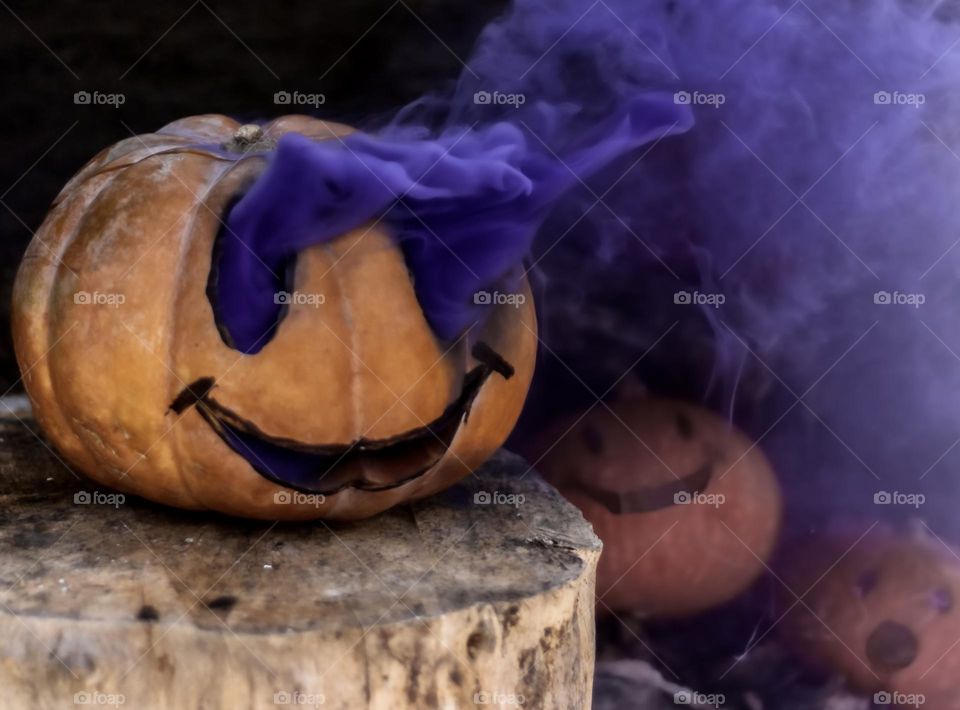 A carved pumpkin with purple smoke billowing from its eyes, smaller pumpkins look on in awe
