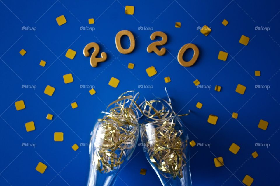 Conceptual flat lay of a champagne toast with glittering gold confetti and the numbers ‘2020’ in gold on a classic blue background - landscape format