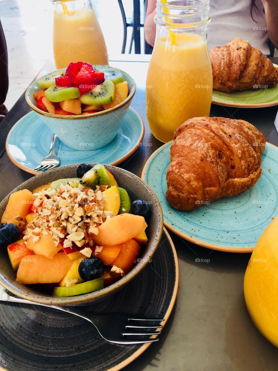 Healthy breakfast, fruit salads, orange juices and croissants served on colorful ceramic dishes and bowls 