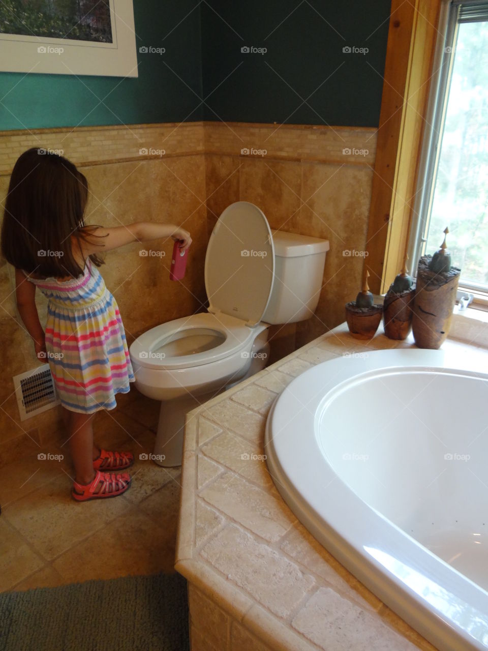 Oops. Little girl holding cell phone over open toilet in bathroom