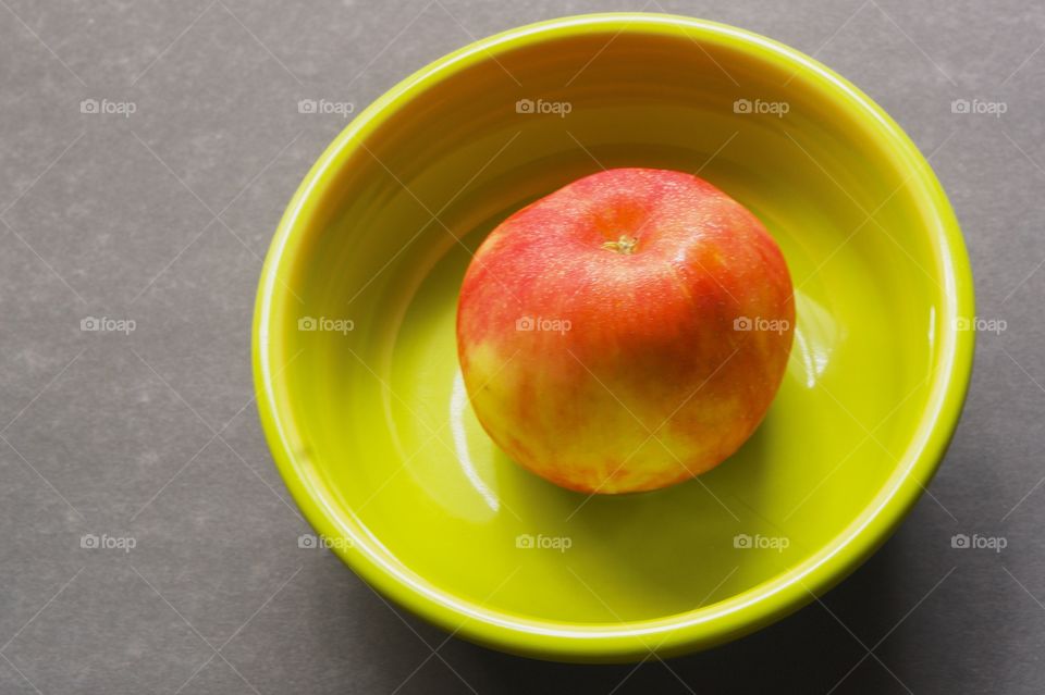 An apple in a green bowl on a gray background
