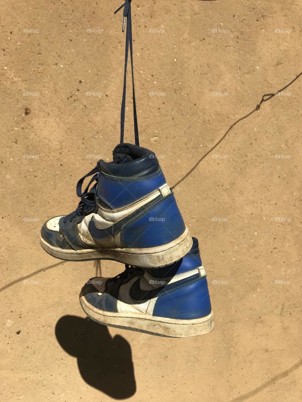 "Suspended from a single string, these sneakers defy gravity as they float in mid-air. The athletic footwear dangles precariously.