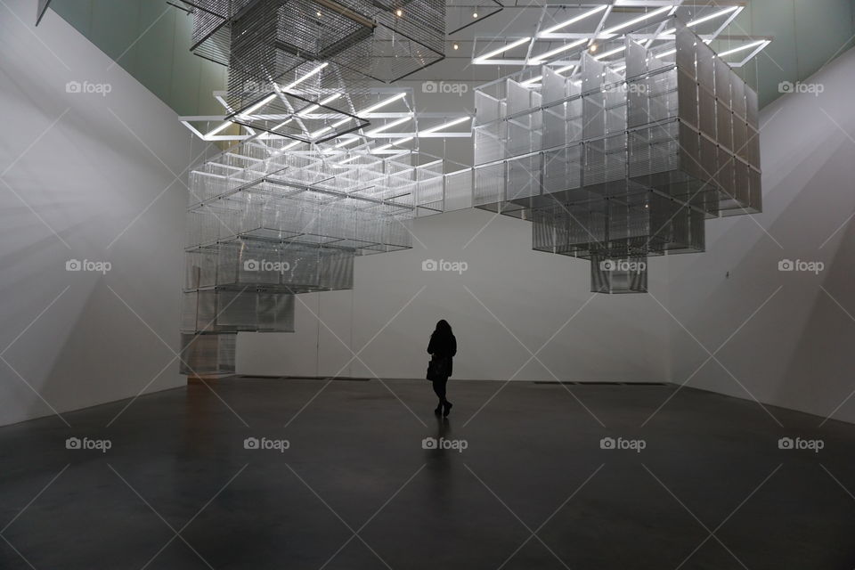 Lone silhouette figure of a young woman walking across an art exhibition room ... captured centrally 