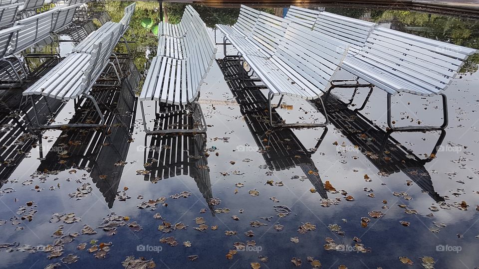 Park benches in a large water puddle after storm in the autumn , höst parkbänkar i en stor vattenpöl 