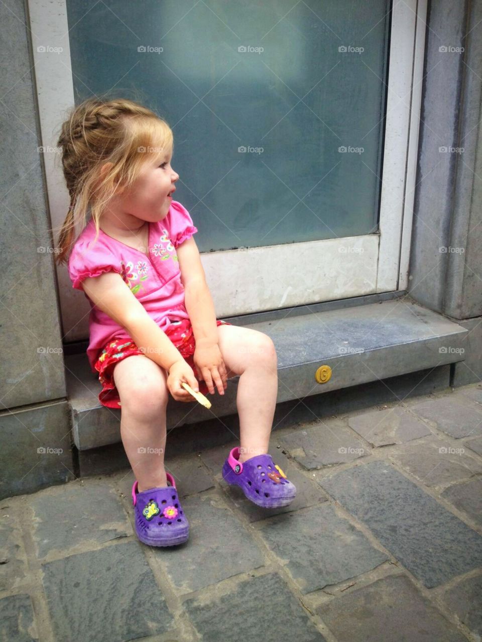 Sweet child enjoying cookie in the summer sun on the doorstep.