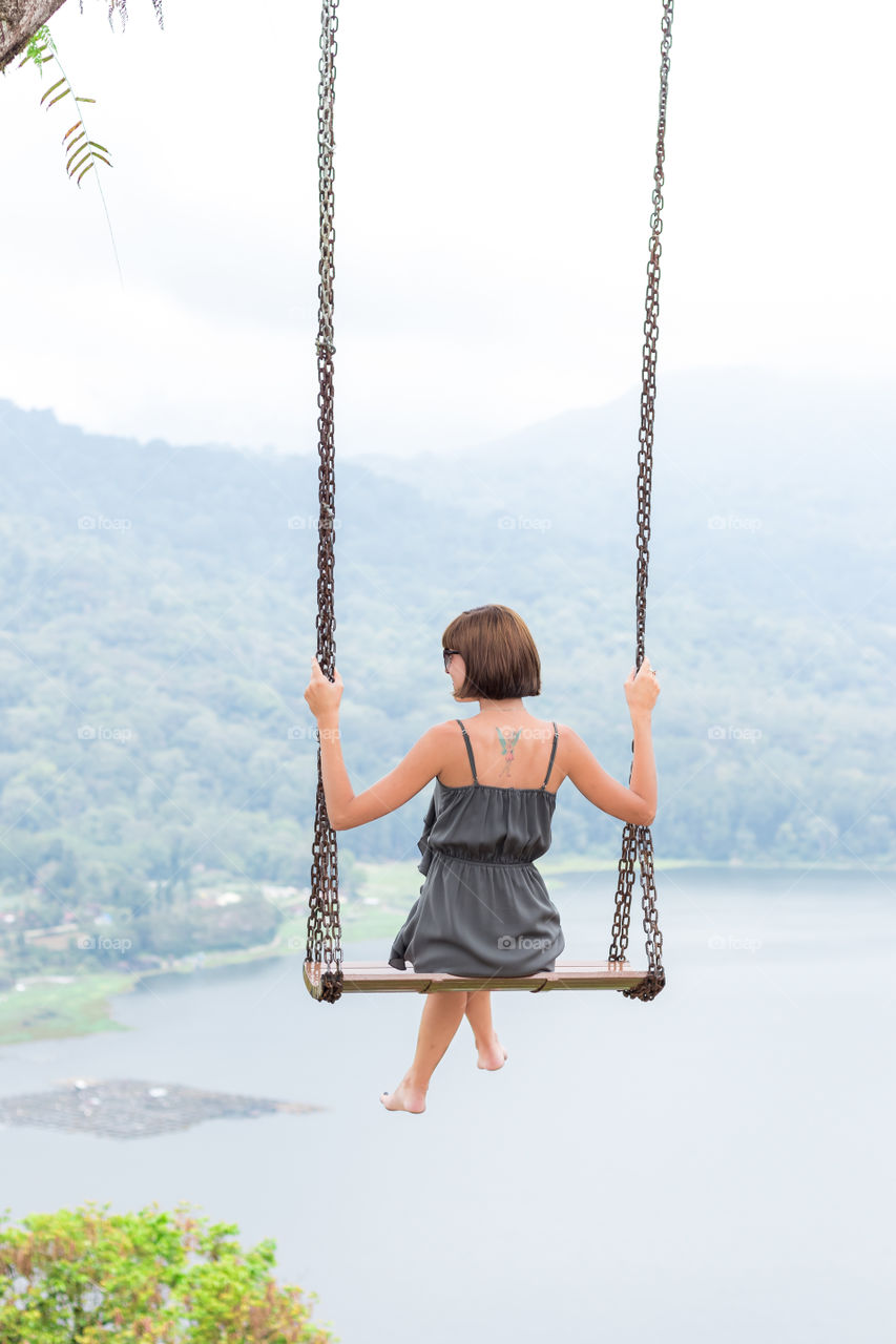 Girl sitting on a swing overlooking the lake and mountains. Bali island.