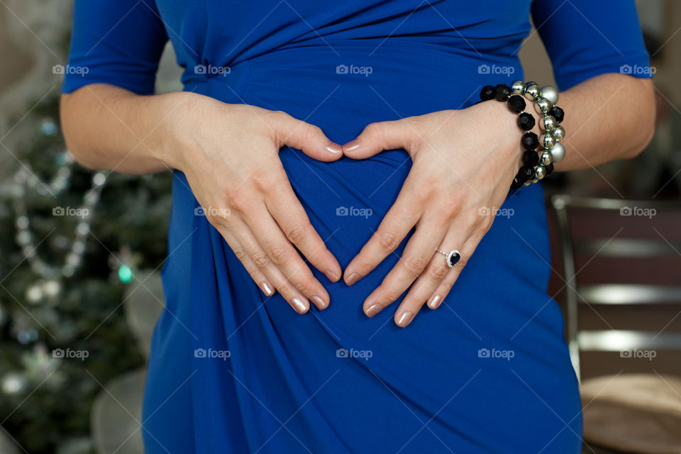Pregnant woman in blue dress hands on stomach 
