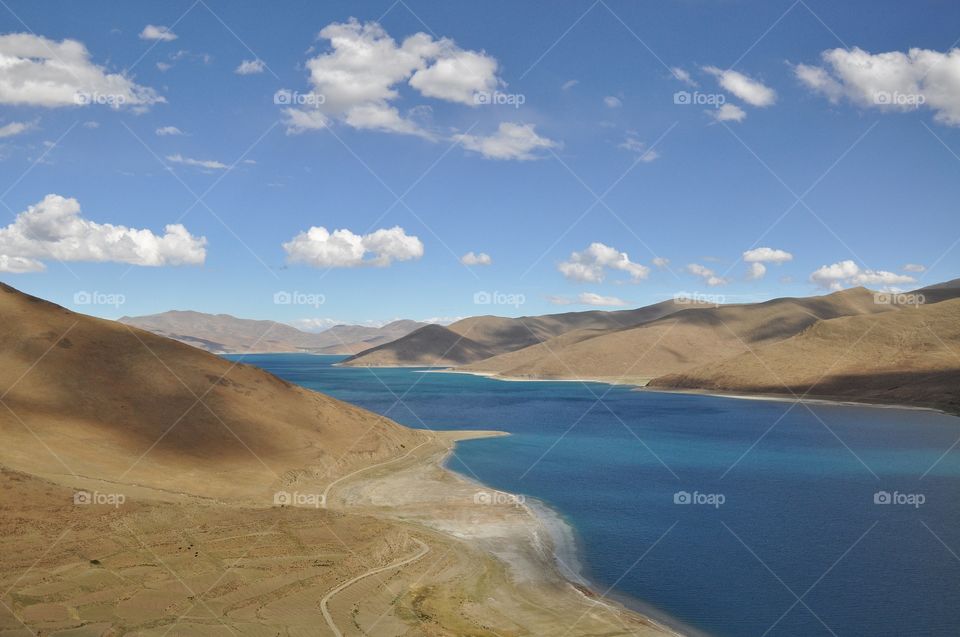 beautiful lake and mountain view in tibet - blue lake surrounded by mountains under the blue cloudy sky