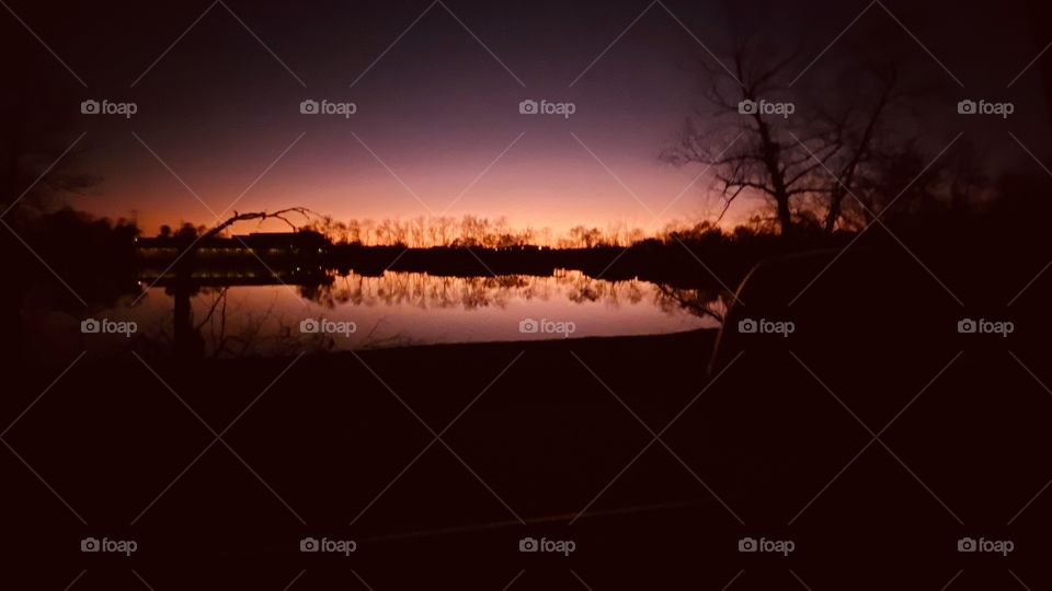 Sunset-Twilight-Night Visible Backlit Skyline. Lake Water Reflections of ShoreLine to Calm Lake Waters. 
