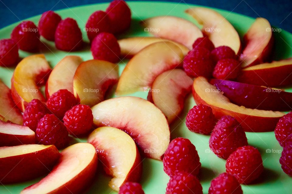 Fruits! - Decorative arrangement of fresh nectarine slices and raspberries on a green plate with green background 