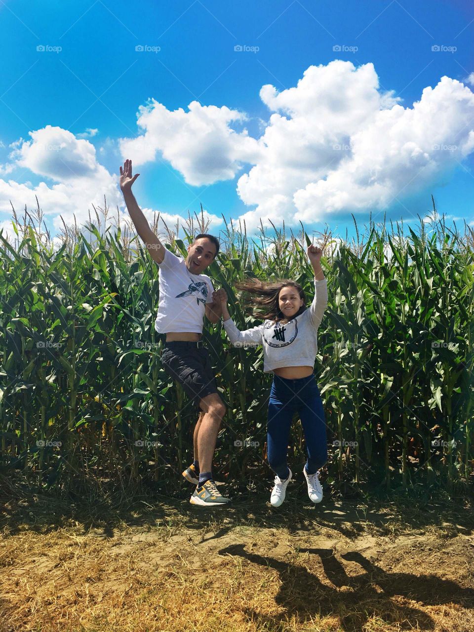 Smiling father and daughter jumping together at the corn field 