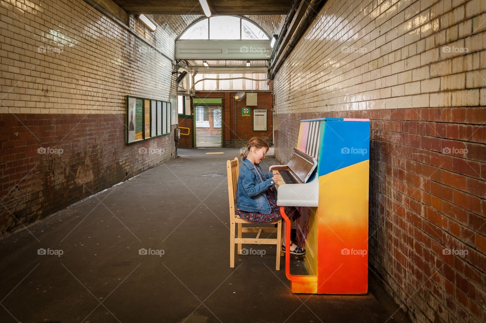 Little girl playing on rainbow painted upright piano in a subway tunnel.