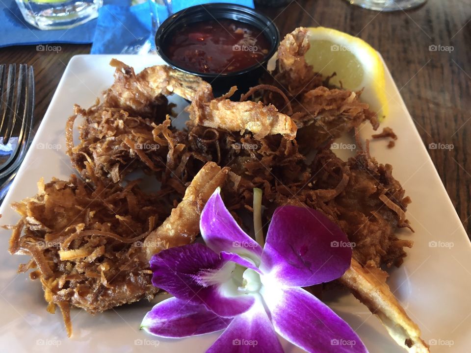 Fried coconut shrimp with dipping sauce and lemon with a decorative orchid flower