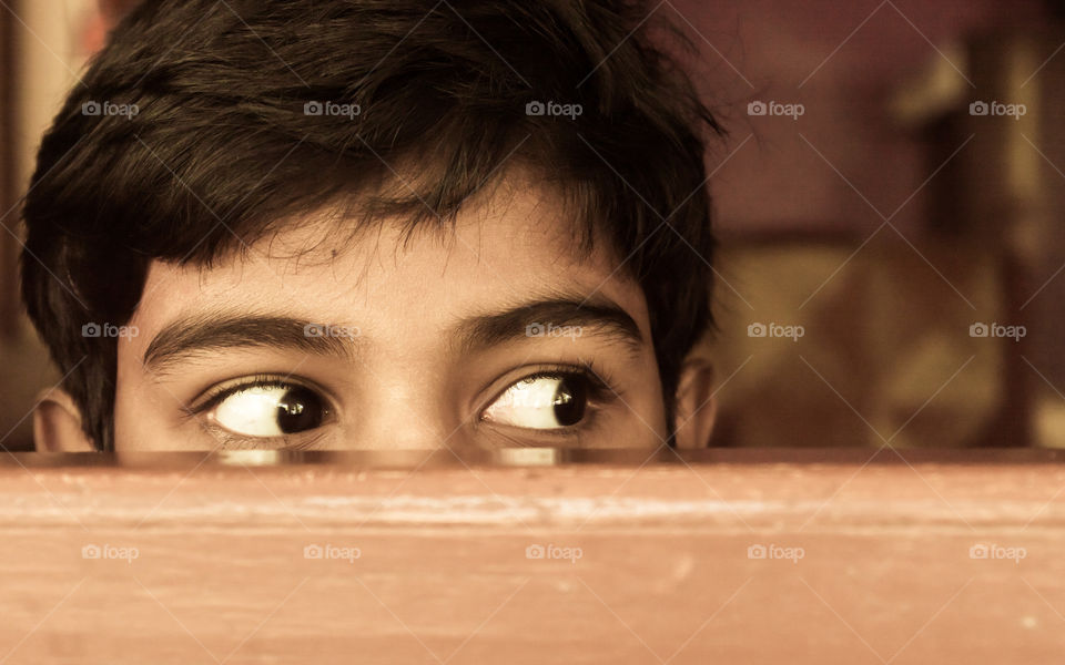 Young boy curiously looking outside through a window.