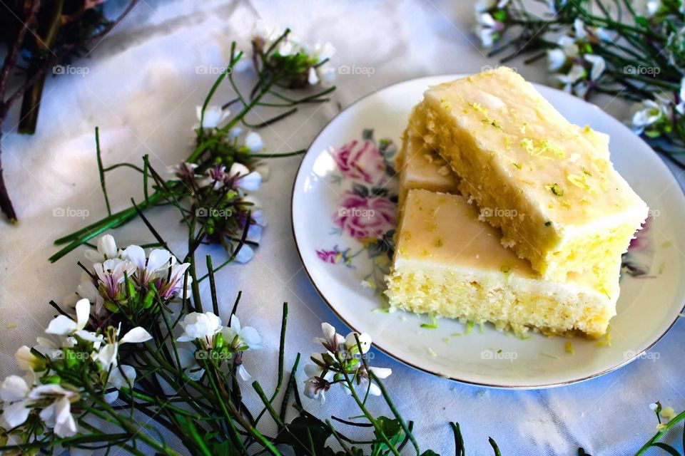 Lemon and lime cake on a floral plate with flowers on the side.