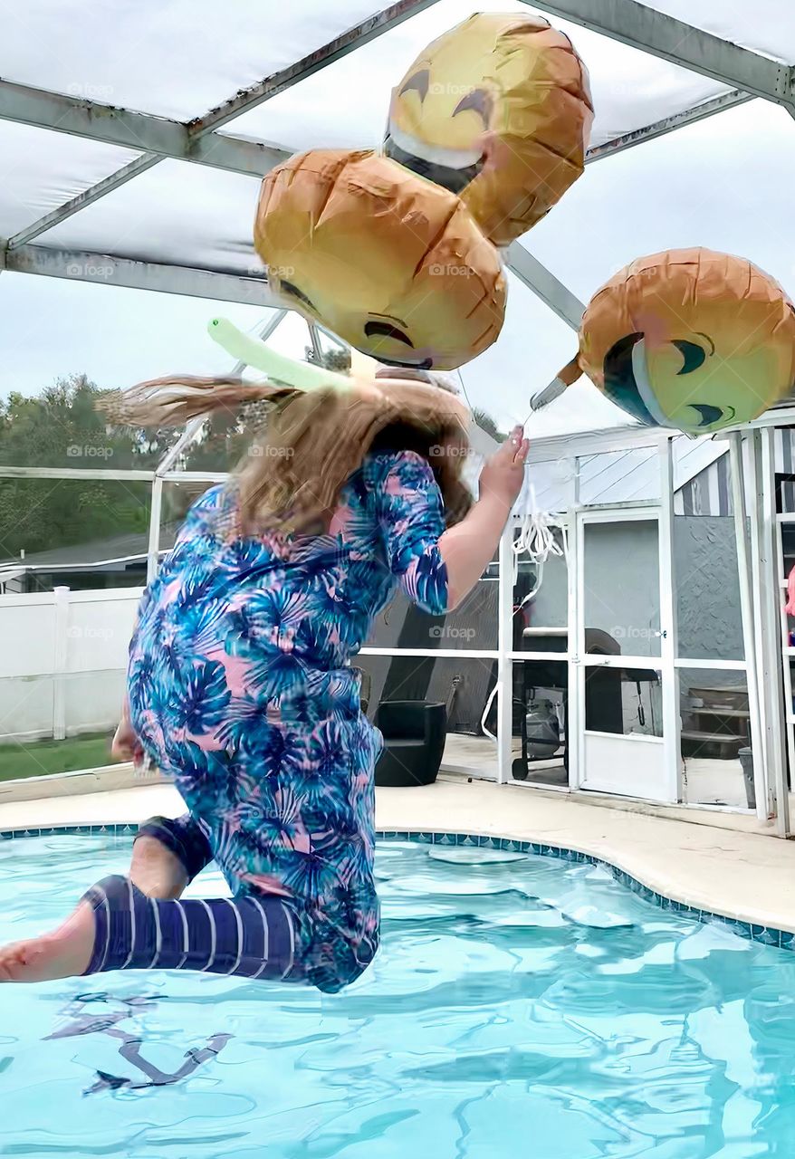 Smiley Faces Helium Balloons Seem To Pull The Girl Up In The Air While She Jumps In The Water With It In The Pool.