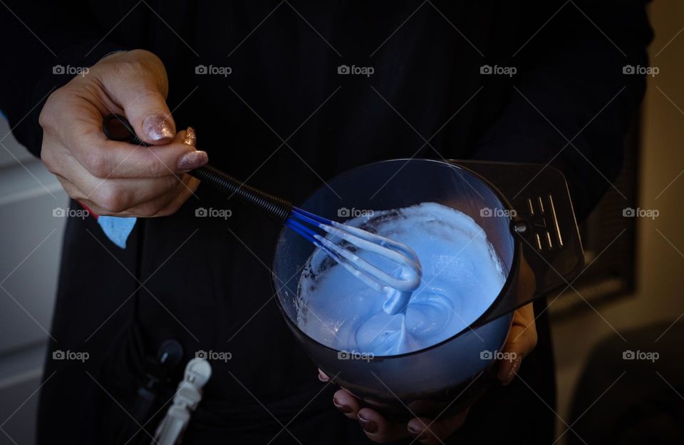A young caucasian girl hairdresser in a black shirt holds a bowl with powder and an oxidizer while bleaching her hair and mixes the mass with a small whisk, top view close-up. The concept of a hairdressing salon, professional services, hair coloring.