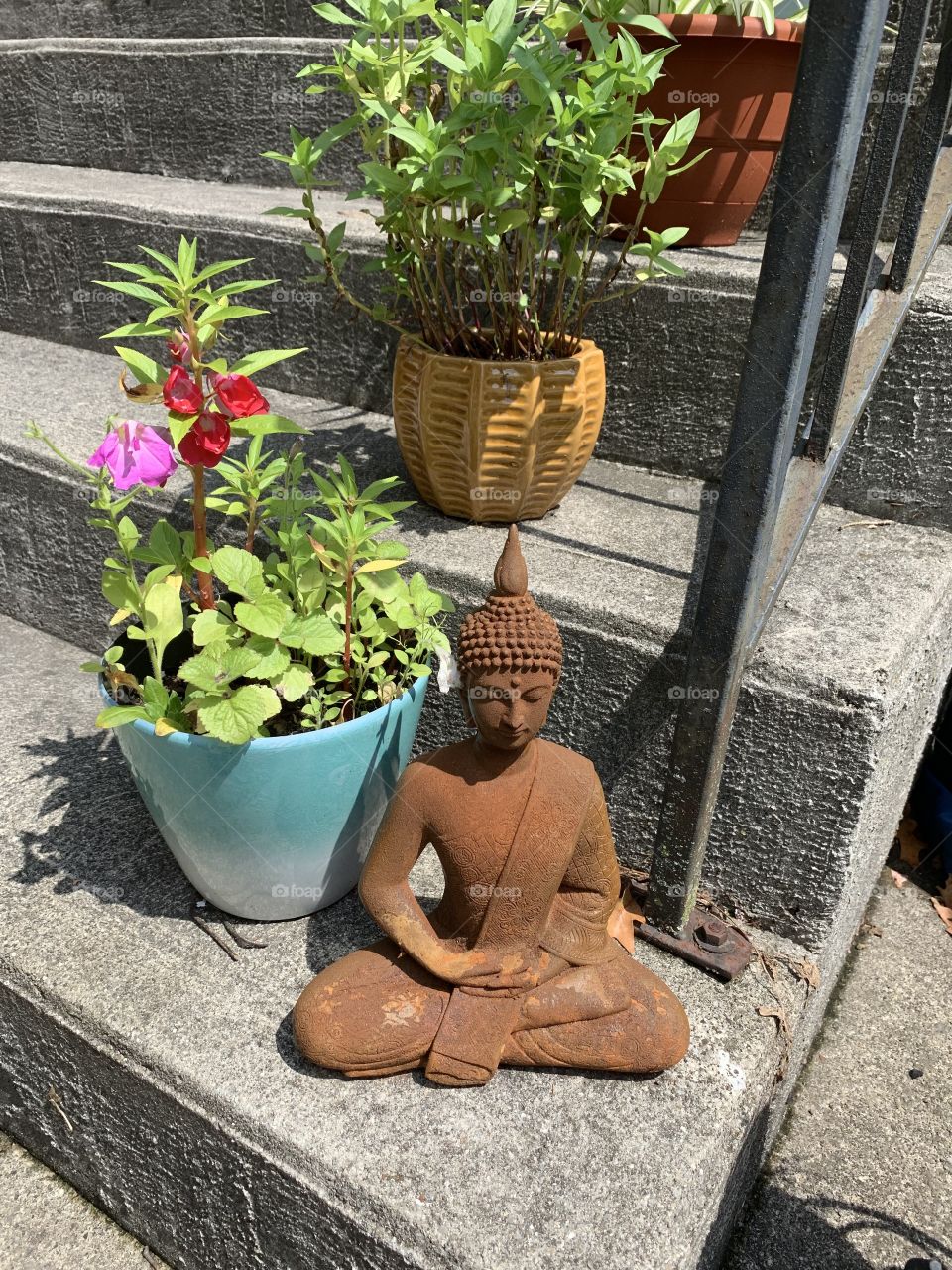 Zen rust statue on concrete patio steps with potted flowers 