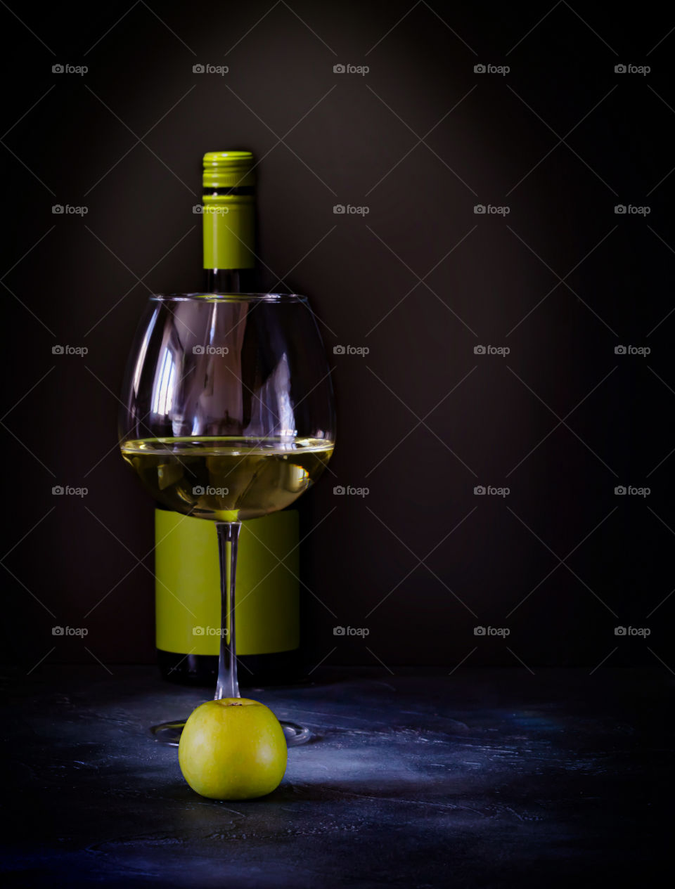 Homemade apple wine. A bottle, a glass of white fruit wine and an apple stand in front of each other on a dark background. Food photo, vertical orientation, copy space