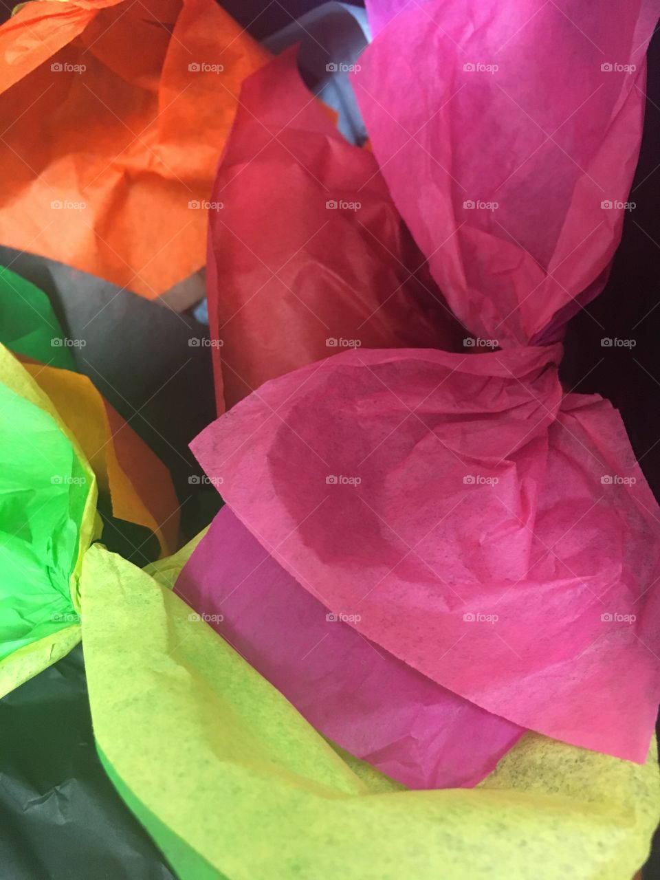 Pieces of craft tissue paper ready to make paper flowers.  Colors include pink, red, orange, green, and yellow.  