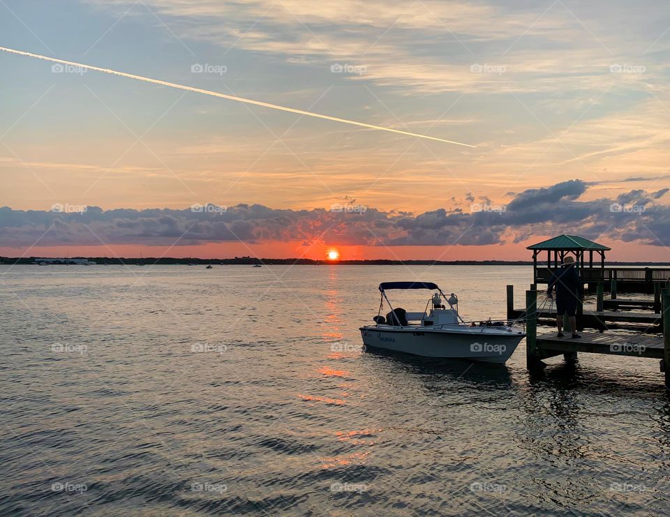 Sunset In The Horizon With Deep Orange Color Sighting With Boat By Dock, By The Island Reflecting On The Water.