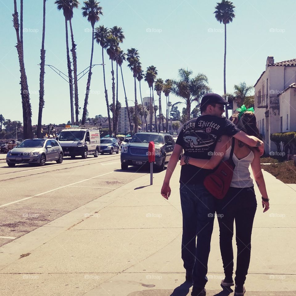 Couple with their Arms Around Eachother Walking Down the Street Lined with Palm Trees