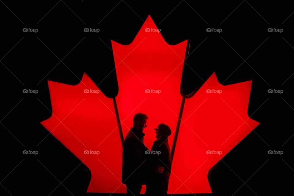Canadian pride; two people in front of Canadian Maple leaf at Nathan Philips square. single focus on deep red maple and silhouettes