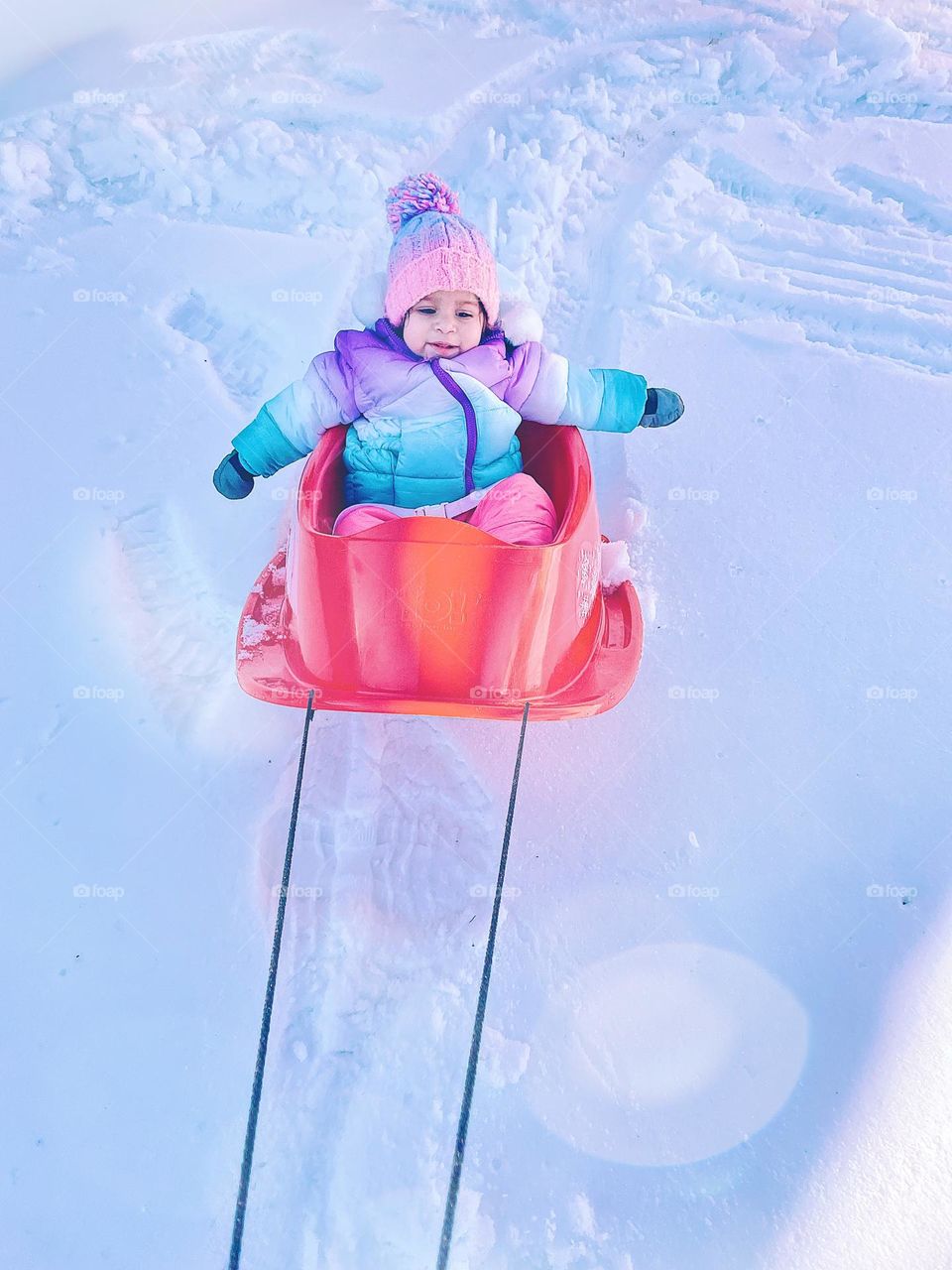 Toddler goes for a sled ride, sledding in the winter time, toddler having fun in the snow, sledding with toddlers, going fast in the sled, mother’s point of view 