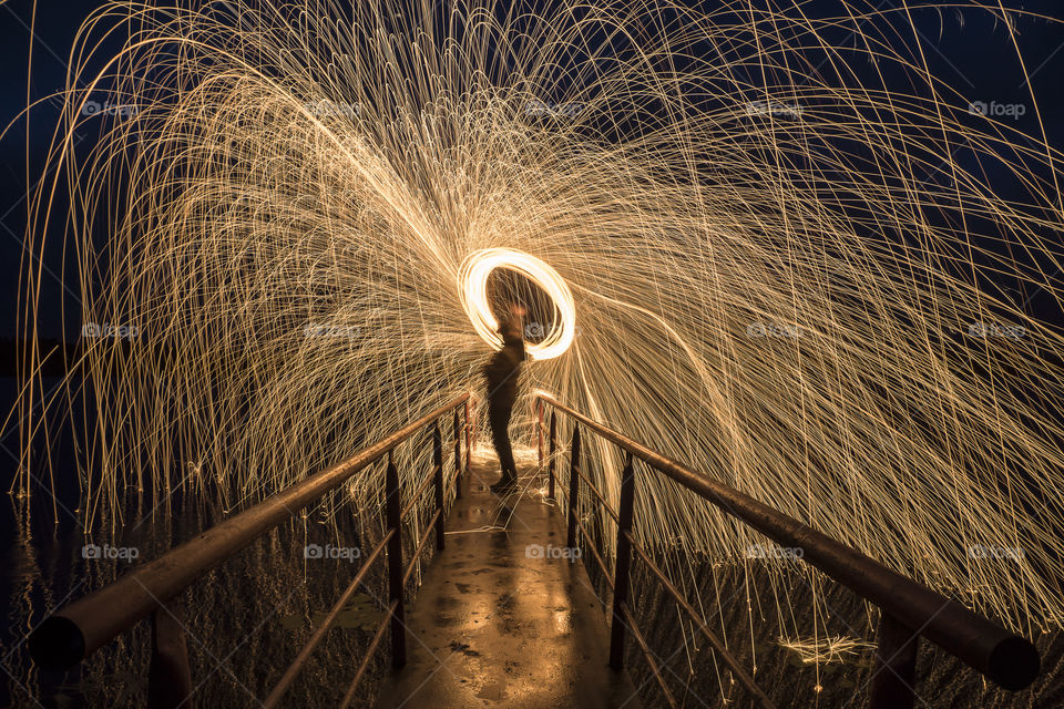Person spinning wire wool on footbridge at night