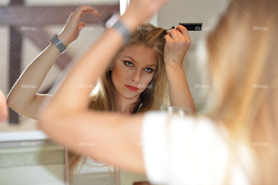 Reflection of blonde woman combing her hair