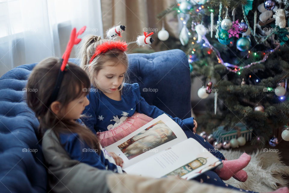 Little sisters reading a book at Christmas time 