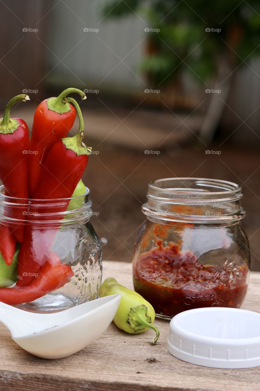 Home canning on the farm of fresh red peppers; outdoor rustic image red peppers chopped and preserves in jar and on white ladle 