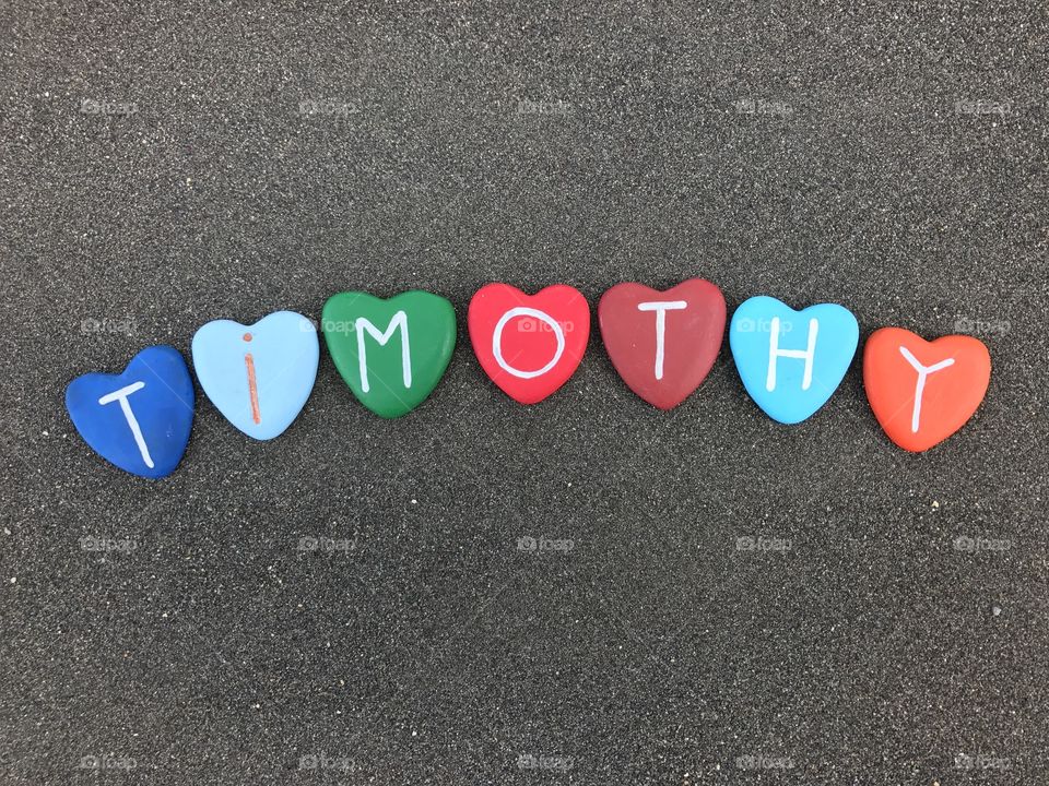 Timothy, masculine name with colored heart stones over black volcanic sand