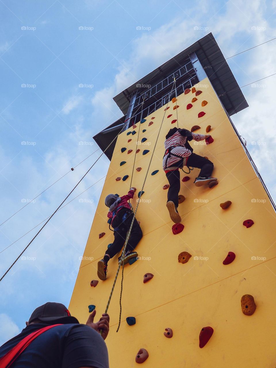 Two girls climbing the outdoor tower against blue sky