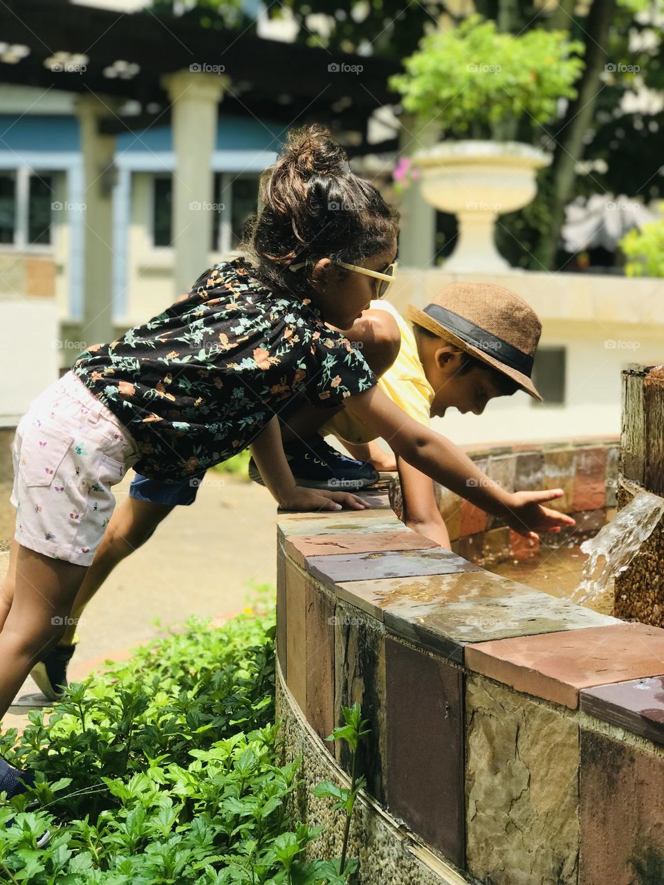 Kids playing at water fountain by wearing summer outfits.