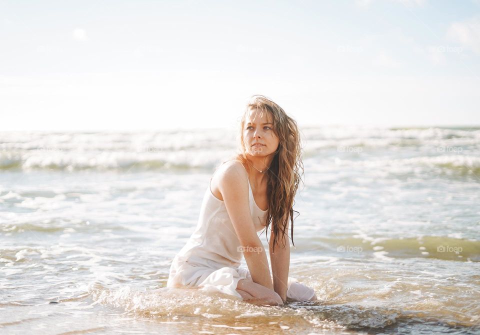 Young blonde beautiful woman with long hair in white dress enjoying life on sea beach