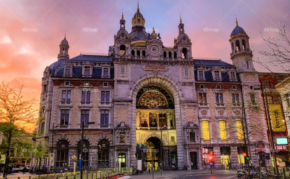 The historic Antwerp central railway station against a dramatic and colorful sunrise sky