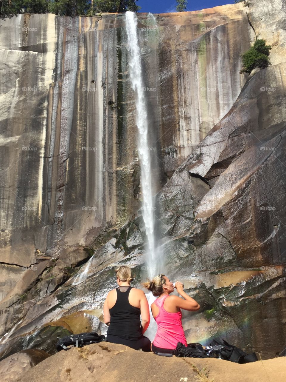Rear view of women sitting on rock in front of waterfall