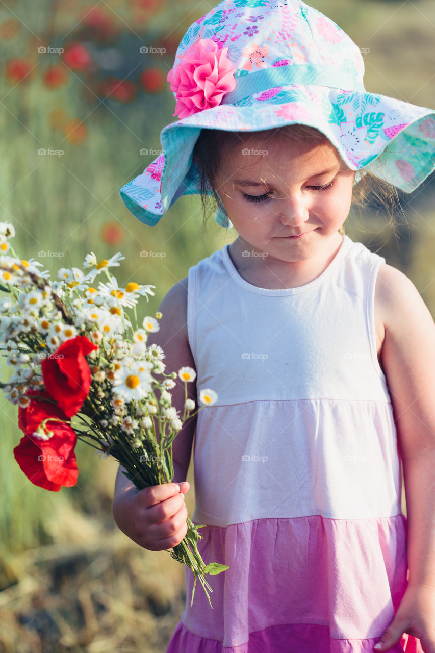 Lovely little girl in the field of wild flowers. Cute girl picking the spring flowers for her mom for Mother's Day in the meadow. Girl holding bouquet of flowers. Spending time close to nature