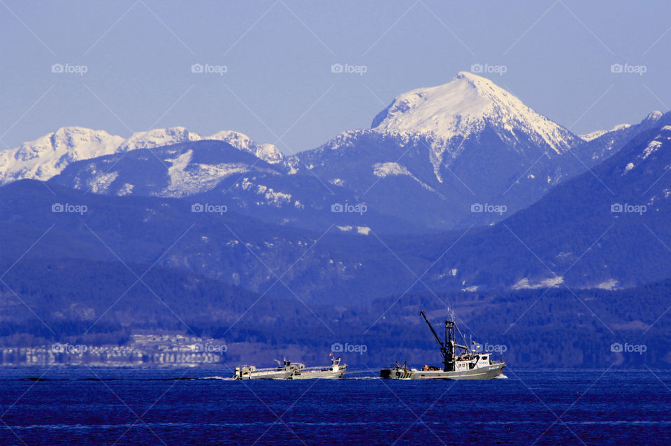 Herring season is prolific in our area on the Pacific Coast and a fishing boat pulling 2 net boats is likely returning home from the harvest. Its another sunny clear day reflecting the sky & ocean making the hills & mountains blue too!