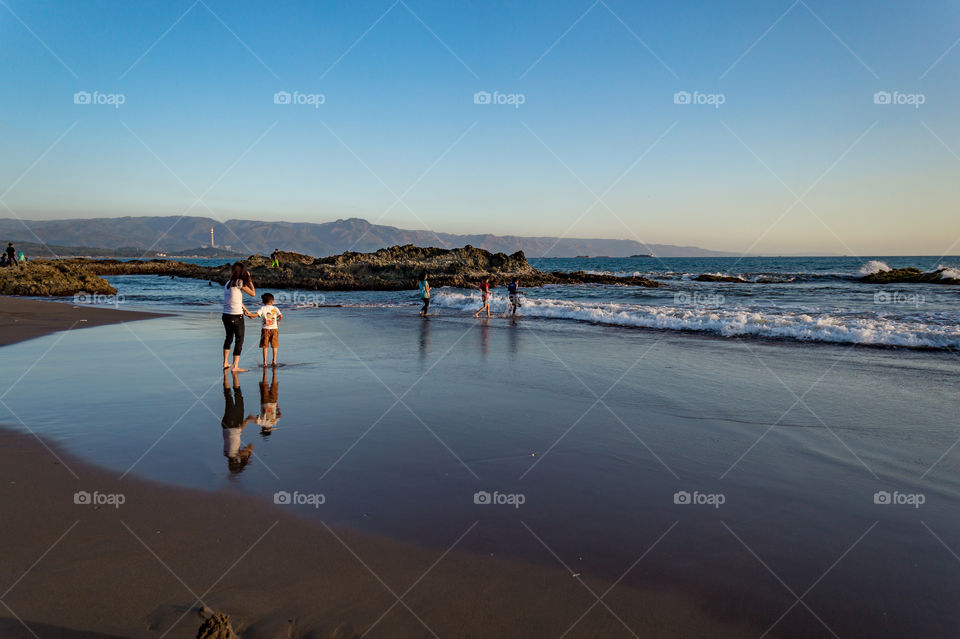 People on the beautiful beach in the afternoon and their reflection, waiting for the sunset