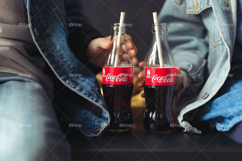 cute guys, brother and sister, move out, rejoice, spend time together and drink Coca-Cola.  children are dressed in denim clothes, black background.  bottles with coca-cola glass