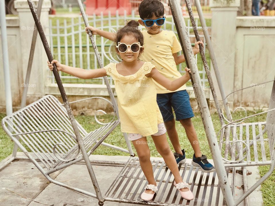 Two kids in a summer outfits and swinging on a swing.