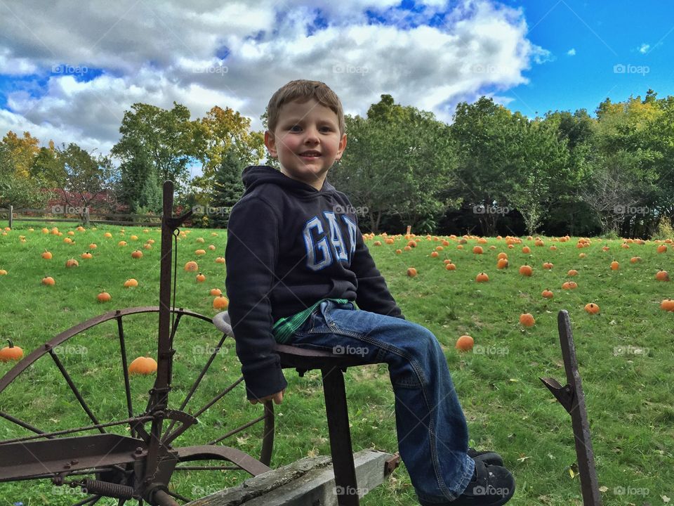 Boy sitting on agricultural equipment in pumpkin field