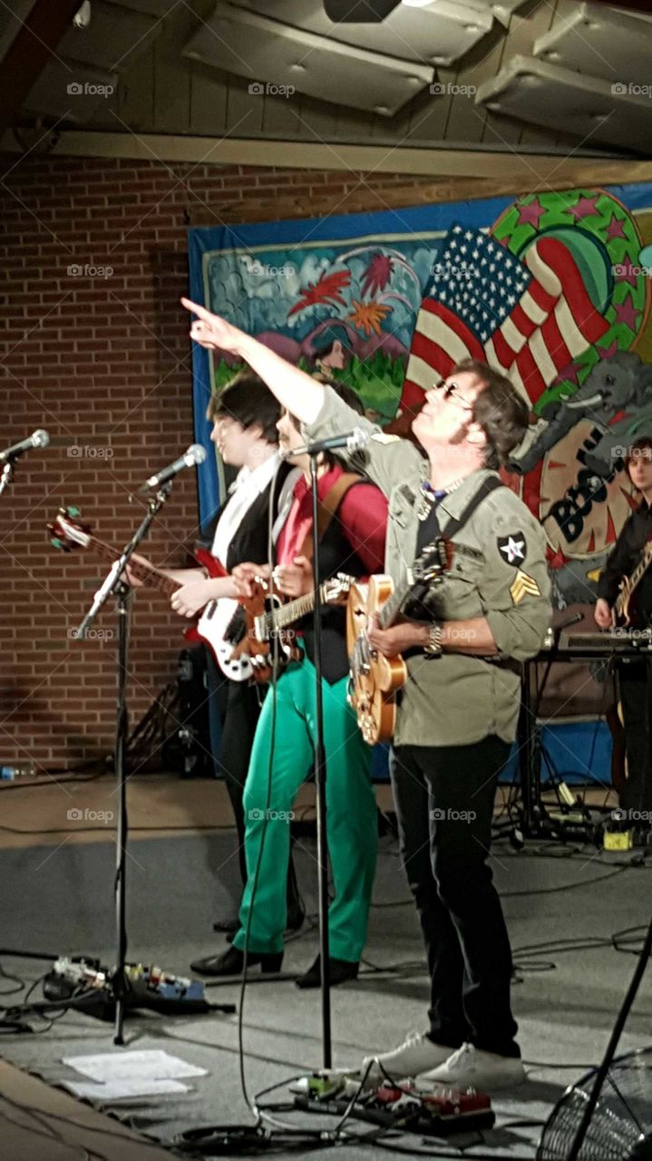 Beatles impersonators pump up the crowd at an outdoor amphitheater with their music.